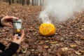 Hand holding phone and taking photo of pumpkin and leaf. instagram blogging concept. halloween or thanksgiving fall holiday.