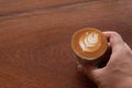 Hand holding Piccolo Latte art in small glass on wooden desk