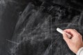 Hand holding piece of chalk against empty dusty blackboard