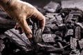 Hand holding piece of charcoal, with background. Dirty coal emitter hand