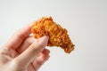 A hand holding a piece of crispy fried chicken with a perfectly golden crust.