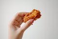 A hand holding a piece of crispy fried chicken with a perfectly golden crust.