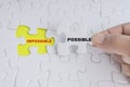 Hand holding piece of jigsaw puzzle with word IMPOSSIBLE POSSIBLE. Royalty Free Stock Photo