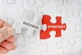 Hand holding piece of jigsaw puzzle with word SUCCESS STRATEGY Royalty Free Stock Photo