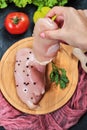 Hand holding piece of raw chicken fillet from wooden plate with fresh vegetables Royalty Free Stock Photo
