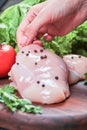 Hand holding piece of raw chicken fillet from wooden plate with fresh vegetables Royalty Free Stock Photo