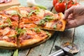 Hand holding piece of rustic thin pizza with arugula, salami and