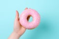 a hand is holding a pink doughnut on a background.