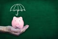 Saving For Rainy Day With Hand Holding Piggy Bank on Chalkboard Background Royalty Free Stock Photo