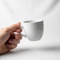 A hand holding a plain white ceramic mug against a neutral background Royalty Free Stock Photo