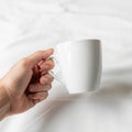 A hand holding a plain white ceramic mug against a soft white background Royalty Free Stock Photo