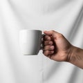A hand holding a plain white ceramic mug against a soft, neutral backgroun Royalty Free Stock Photo
