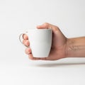 A hand holding a plain white ceramic mug against a white background Royalty Free Stock Photo