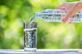 Hand holding plastic bottle water and pouring water into glass on wooden table on blurred green bokeh background Royalty Free Stock Photo