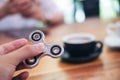 A hand holding and playing metal silver color fidget spinner with coffee cups and people using mobile phone Royalty Free Stock Photo