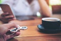 A hand holding and playing metal silver color fidget spinner with coffee cups and people using mobile phone Royalty Free Stock Photo