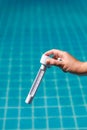 Hand holding pool thermometer above clear blue swimming pool water, checking temperature during routine pool maintenance Royalty Free Stock Photo