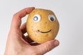 Hand holding potato smiley with Googly eyes. Food with funny face on white background