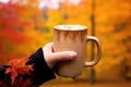 hand holding pumpkin spice latte mug in front of autumnal background