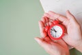 Hand holding red analog alarm clock with blurred calendar and green background, timeline, punctual, appointment