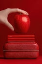 Hand holding a red apple with matching books and case on a red background Royalty Free Stock Photo