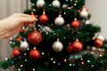 hand holding red ball ornament close up decorating christmas tree at home on background of festive tree with colorful lights. spa Royalty Free Stock Photo