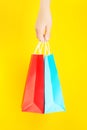 Hand holding red and blue shopping or gift bag against yellow background Royalty Free Stock Photo