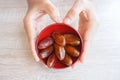 Hand holding red bowl with dried fruits from date palm on wooden background, phoenix dactylifera on red bowl in hand