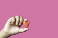 Hand holding a red candy shape heart on a pink background with clipping path for Valentine`s Day