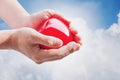 Hand holding red hart on blue sky and white clouds, with bright light Royalty Free Stock Photo