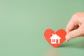 Hand holding red heart with home sign on green background for family home, homeless shelter and real estate, housing and mortgage