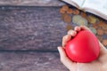 Hand holding red heart over a wooden table with open holy bible book and coins Royalty Free Stock Photo