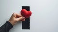 hand holding a red heart-shaped object against a background with a black rectangle in the center.AI generated image Royalty Free Stock Photo