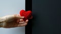 hand holding a red heart-shaped object against a background with a black rectangle in the center.AI generated image Royalty Free Stock Photo