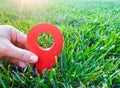 A hand is holding a red location marker in the green grass. The concept of tourism and travel. Navigation and exploration.