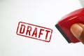Hand holding a red rubber stamp with a red DRAFT ink imprint on a white paper background. Conceptual image representing Royalty Free Stock Photo