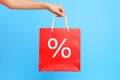 Hand holding red shopping bag with percentage sale sign on blue background Royalty Free Stock Photo