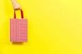 Hand holding red striped present gift bag over yellow background. Shopping, holiday, donation concept Royalty Free Stock Photo