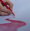 Hand holding a red watercolor pencil, drawing on white paper. Royalty Free Stock Photo