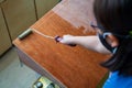 Hand holding roller and applying polyurethane on the wooden board by a young girl