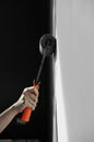 Hand holding roller paint applying grey paint on white wall. Royalty Free Stock Photo
