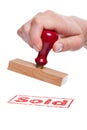 Hand holding a rubber stamp with the word Sold