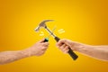 Hand holding screwdriver fighting with hand holding hammer on yellow background Royalty Free Stock Photo