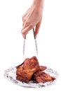 Hand holding serving roasted chicken in aluminum foil with tongs. Food and appetizer concept. Kitchen and cooking theme. Delicious