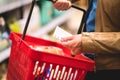 Hand holding shopping list and basket in grocery store aisle.