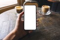 A hand holding and showing black mobile phone with blank white screen and coffee cup on wooden table Royalty Free Stock Photo