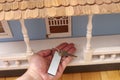 Hand with key and tag on a white wooden front porch of a big blue wooden doll house