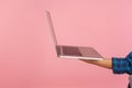 Hand holding silver laptop, closeup of computer gadget against pink background, internet advertising concept Royalty Free Stock Photo