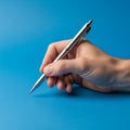 A hand holding a silver metallic pen against a solid blue background Royalty Free Stock Photo