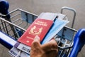 Hand holding Singapore passport, mask and boarding pass, holding on to airport trolley Royalty Free Stock Photo
